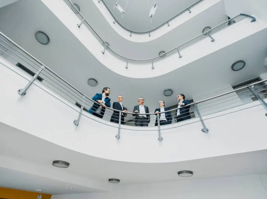 Partner von Stecker Berger + Partner stehen am Geländer im 1. Stock des Firmengebäudes in Kassel
